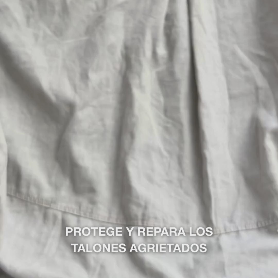 Primer plano de una mano tomando una porción cremosa y densa de la textura Heel Repair y masajeándola suavemente en piel seca y agrietada del talón: la consistencia espesa se absorbe visiblemente, suaviza e hidrata las zonas ásperas, mientras la urea al 25 %, manteca de karité y aceite de árbol de té calman y protegen la piel.