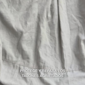 Primer plano de una mano tomando una porción cremosa y densa de la textura Heel Repair y masajeándola suavemente en piel seca y agrietada del talón: la consistencia espesa se absorbe visiblemente, suaviza e hidrata las zonas ásperas, mientras la urea al 25 %, manteca de karité y aceite de árbol de té calman y protegen la piel.