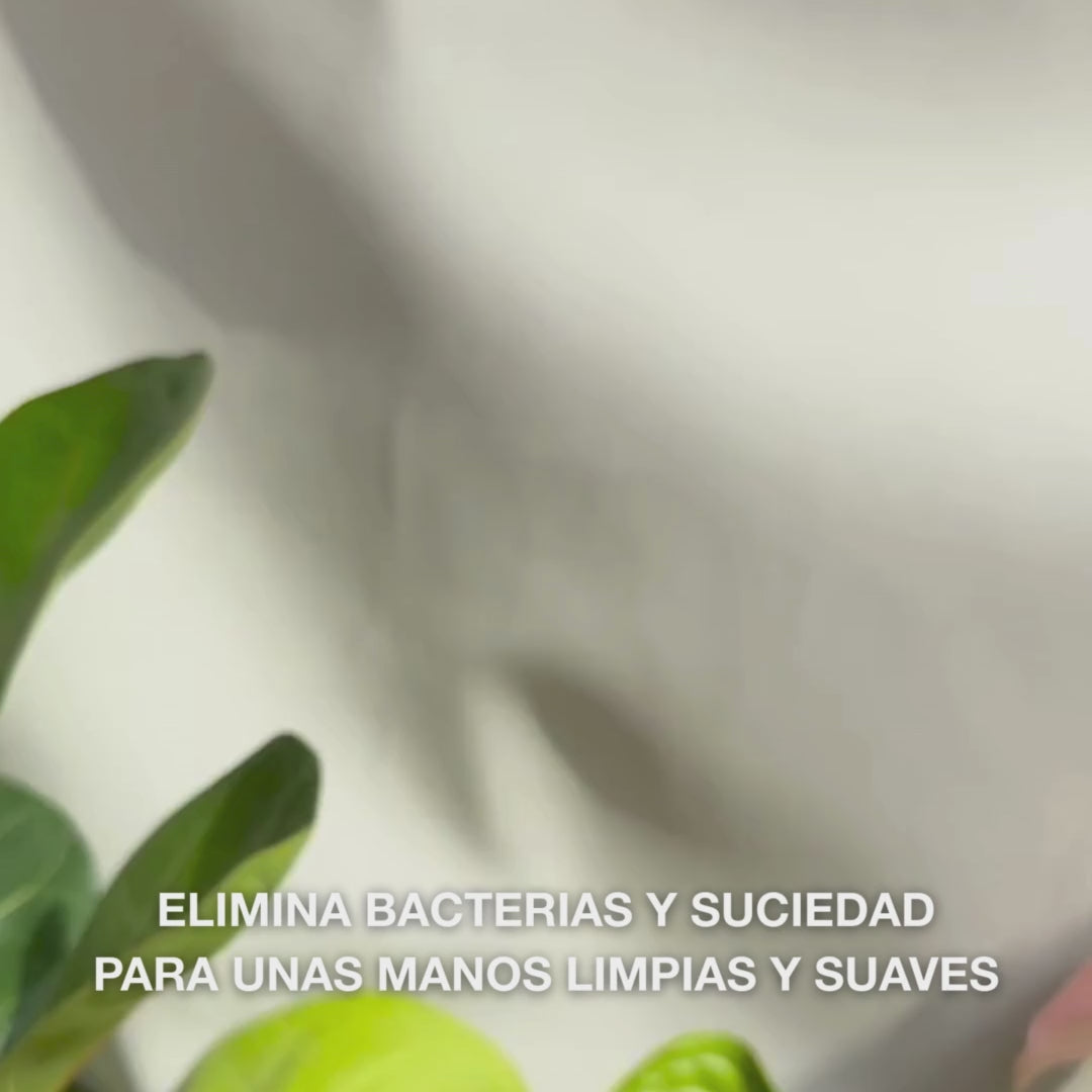 Primer plano de manos que dispensan un jabón líquido transparente de tono azul claro, espumoso y enriquecido con Tea Tree Oil, en la palma, y luego lo extienden suavemente sobre palmas, dorso de las manos y entre dedos—mostrando la espuma suave que limpia bacterias y suciedad mientras suaviza e hidrata la piel.