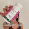 Primer plano de una mano sosteniendo el suplemento alimenticio de Vitamina B12, abriendo la tapa y vertiendo cápsulas blancas y lisas—mostrando el producto para uso diario que apoya la energía, el sistema inmunitario, el sistema nervioso y reduce el cansancio.